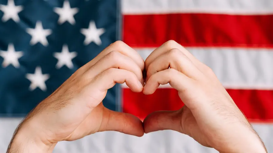 Two hands forming a heart shape in front of an American flag